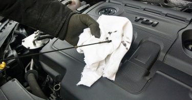 Fotografía de una mano limpiando una varilla con un trapo para verificar el aceite del motor.