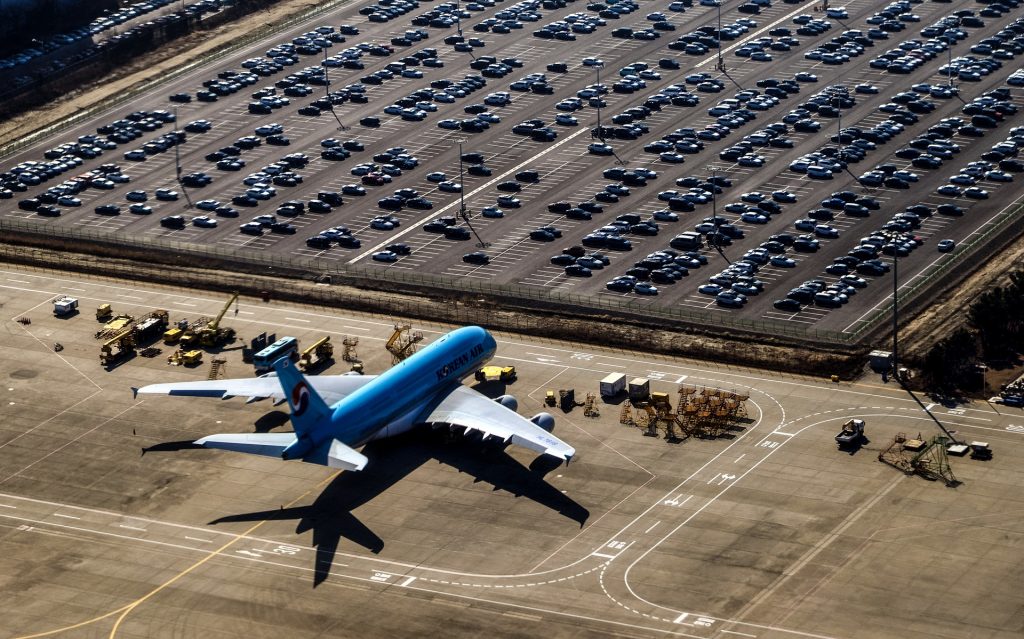 Parking de un aeropuerto, junto a un avión aparcado en la pista.