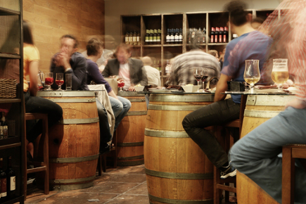 Fotografía en el interior de un restaurante/taberna, con gente tomando una cerveza/vino, en mesas en forma de barril. Muy típico!