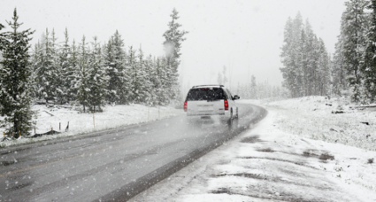 Fotografía de un coche en la carretera, en invierno con nieve en los lados de la carretera.